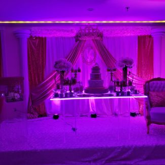 Custom wedding reception dessert set up on a stage with up lighting and backdrop